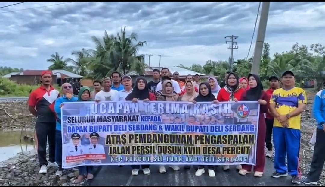 Warga Dusun XVIII Persil berfoto bersama dengan memegang spanduk ucapan terima kasih untuk menyambut penuh sukacita rampungnya pengaspalan Jalan Persil. (Dok. Diskominfostan Deli Serdang)